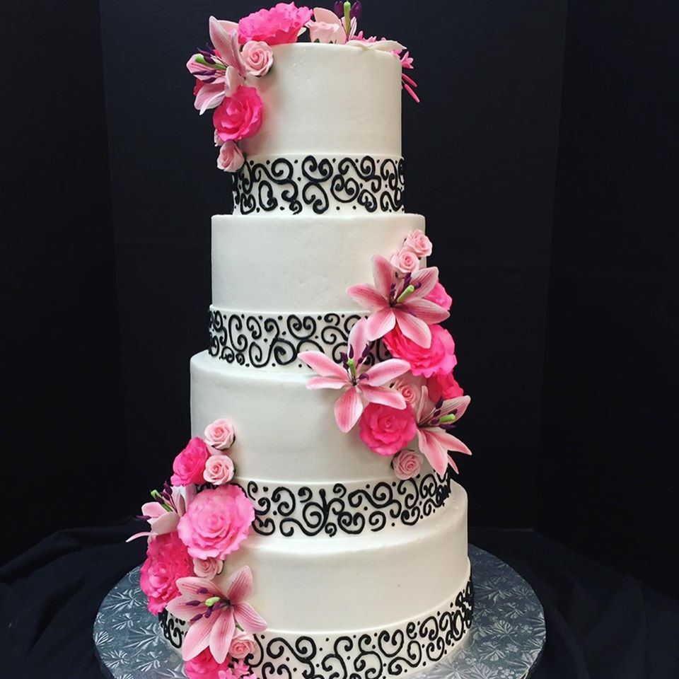 A four-tier white wedding cake with black scroll piping and pink sugar flowers